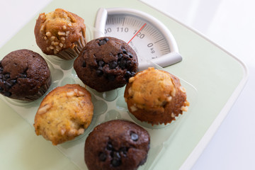 Cupcakes that are high in calories, put on the scales and show a very high weight. Delicious but have a negative effect on the body in terms of sugar and fat. Concept of unhealthy food with copy space