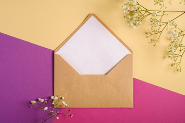 Kraft brown paper envelope with white empty card, gypsophila flowers, purple and cream yellow...