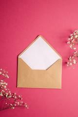 Kraft brown paper envelope with white empty card, gypsophila flowers, red pink background, mockup template