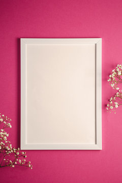 White picture frame with empty template, gypsophila flowers, pink red background, mockup card