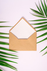 Kraft brown paper envelope with white empty card on palm leaves, white background, mockup blank letter