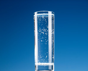 Glass of water with carbon dioxide bubbles on a blue background