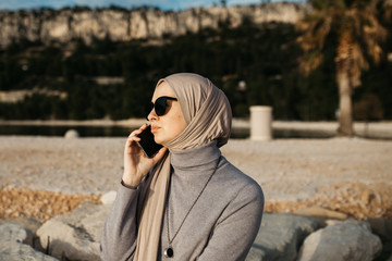 Beautiful portrait of young European Muslim women with hijab holding mobile phone and talking on the phone. She is happy and relaxed.