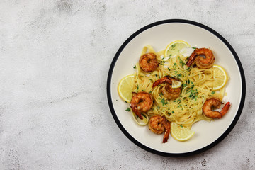 Fried prawns with tagliatelle in cream sauce in a plate on a light background. Top view, flat lay