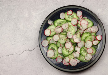 Cucumber and radish salad in a plate on a light background. Top view, flat lay