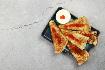 Pancakes with caviar and sour cream in a plate on a light background. Top view, flat lay