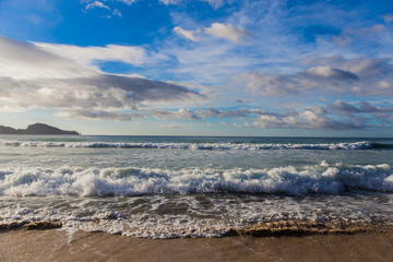 empy sand beach with wawes and sun covered with cloudy sky and tropical trees on background in El Nido, Palawan province, Philippines