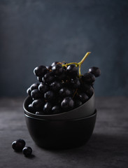 a cluster of juicy black grapes lies in a dark gray bowl on a dark gray table