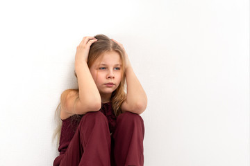 A young girl  sits on the floor by the wall and thinks or sad about something