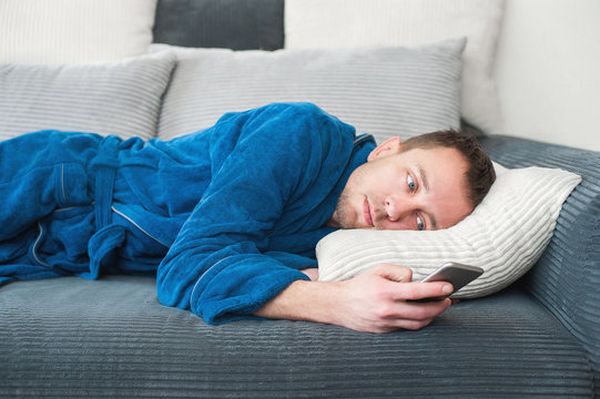 A Man Lies On The Couch, Bored And Looks At The Phone