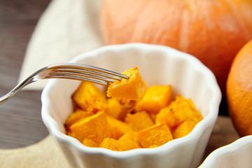 Baked pumpkin piece on fork, vegatables, white ceramic bowl on blurred background