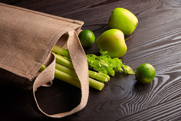 Reusable shopping jute bag with fresh fruits and greens on wooden background