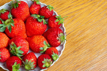 Fresh strawberries in white porcelain plate on wooden table