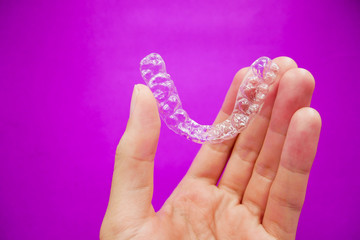 hand holding clear plastic retainer teeth that isolated on purple  background. it's an equipment for orthodontist give the patient to orthodontic surgery in dental clinic or hospital