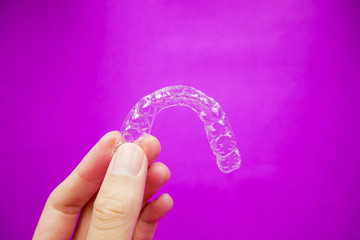 hand holding clear plastic retainer teeth that isolated on purple  background. it's an equipment for orthodontist give the patient to orthodontic surgery in dental clinic or hospital