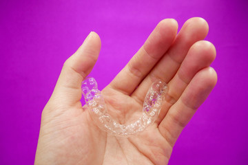 hand holding clear plastic retainer teeth that isolated on purple  background. it's an equipment for orthodontist give the patient to orthodontic surgery in dental clinic or hospital