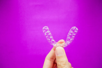 hand holding clear plastic retainer teeth that isolated on purple  background. it's an equipment for orthodontist give the patient to orthodontic surgery in dental clinic or hospital