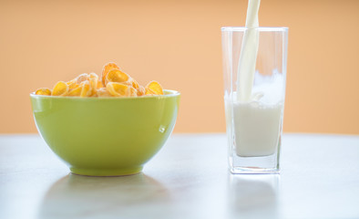 cornflakes in the green dish, milk is flowing into the glass