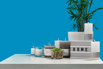 White table with green plant and succulent in pots, some different sized and colors candles, lamp...