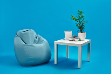 Turquoise armchair bean bag and white coffee table with green flower in a pot, three candles and...