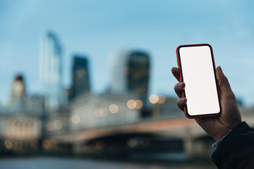 Female hand holding smartphone with white blank screen in the city. Mobile application mockup template.