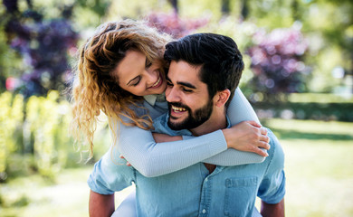 Fototapeta premium Meeting in the park. Boyfriend carrying his girlfriend on piggyback. Love, dating, romance