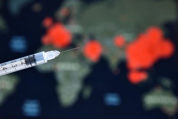 Syringe with a vaccine on blurred world map with corona virus spread marks on background. Stop epidemic. Coronavirus disease named COVID-19. Healthcare concept 
