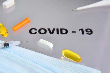 Inscription COVID-19 on display with pills, syringe, thermometer and protection mask on background....