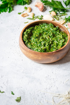 Homemade pesto sauce in a wooden bowl and ingredients for cooking on a gray background close-up, free space for text. Italian food, copy space.