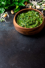 Homemade pesto sauce in a wooden bowl and ingredients for cooking on a black background close-up, free space for text. Italian food, copy space.