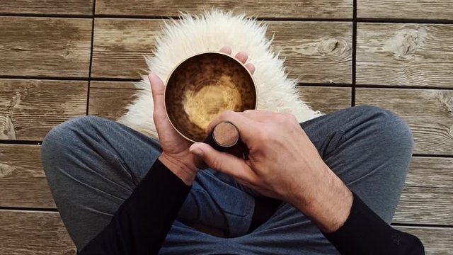 Uomo che suona una campana tibetana seduto a gambe incrociate su background di assi di legno
