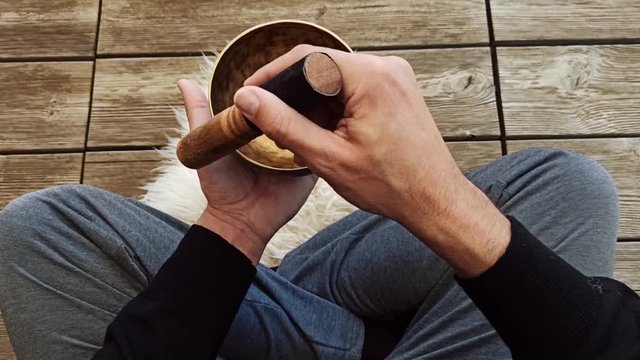 Uomo che medita suonando una campana tibetana seduto a gambe incrociate su pavimento in legno