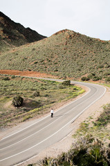 .young man with skateboard skating on a long road in a mountainous landscape