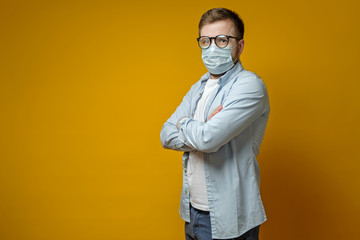 Fototapeta premium Calm man in a medical mask and glasses, standing with arms crossed and looking at the camera, with copy space.
