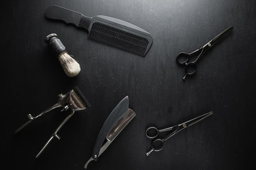 On a black dusty surface are old barber tools. Vintage manual hair clipper comb razor shaving brush shaving brush hairdressing scissors.