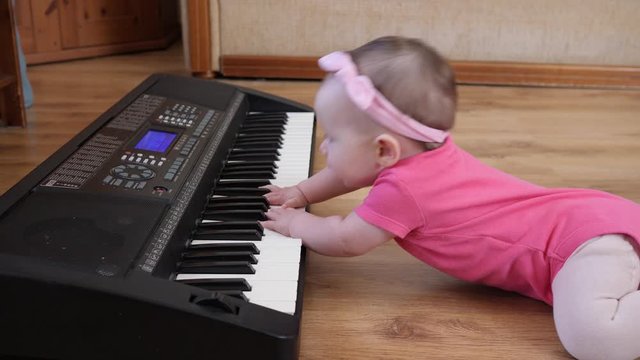 Funny baby toddler playing piano synthesizer crawling the floor at home wearing pink