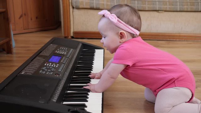 Funny baby toddler playing piano synthesizer crawling the floor at home wearing pink