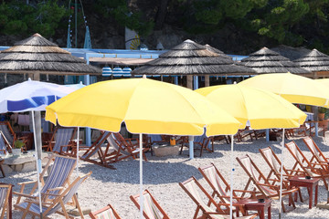 Yellow beach umbrellas and chaise for relax and comfort on sea coast. Happy summer vacations and tourism concept. Paid service on waterscape beaches.