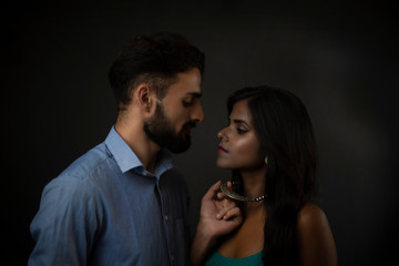 A dark skinned Indian/African girl and a Kashmiri/European/Arabian man in formal wear enjoying themselves in front of a black copy space studio background. Indian lifestyle and fashion photography.