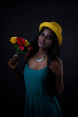 Fashion portrait of young dark skinned Indian/African brunette girl in green western dress, jewelry and yellow hat in front of black copy space studio background. Indian fashion photography.