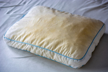 Old dirty used yellow sweat stained pillow on a mattress. Condition of the pillow used for a long time.