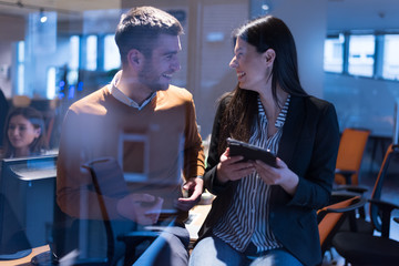 Two focused young business colleagues talking over a digital tablet while having a meeting together in a modern office