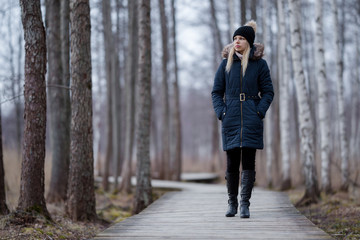 One young woman in dark warm clothes slowly walking on wooden trail at natural park. Cold overcast...