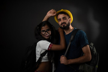 A dark skinned Indian/African girl in school uniform and a Kashmiri/European/Arabian man in casual wear and hat with bag pack in front of black copy space studio background. Indian lifestyle.