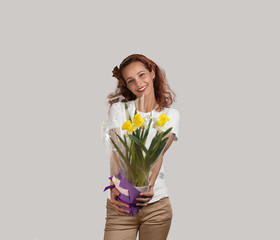 Caucasian attractive girl with a smile on her face extends to the viewer a bouquet of narcissists. Woman has tan skin and a slender figure. Light background
