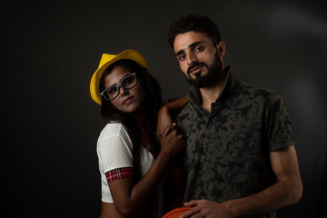 A dark skinned Indian/African girl in school uniform and hat and a Kashmiri/European/Arabian man in casual wear with basket ball in front of black copy space studio background. Indian lifestyle.