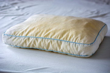 Old dirty used yellow sweat stained pillow on a mattress. Condition of the pillow used for a long...