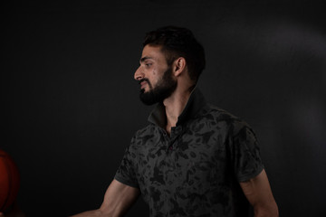 Portrait of young brunette Indian/European/Arabian/Kashmiri man in casual tee shirt whirling a basket ball in hand in black copy space studio background. Indian lifestyle.