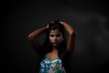 Fashion portrait of a  dark skinned young Indian/African girl in western floral dress in front of a dark copy space studio background. Indian lifestyle.