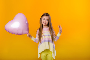 portrait of a happy child girl smiling holding a pink balloon in the shape of a heart